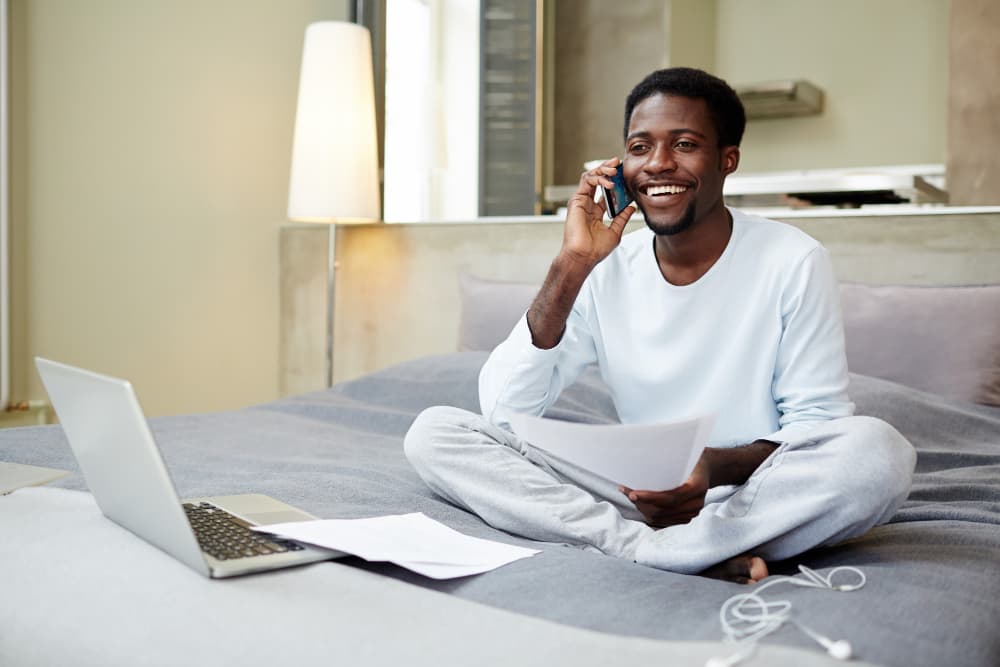 A man sitting on a sofa, smiling on the phone with paperwork in his lap